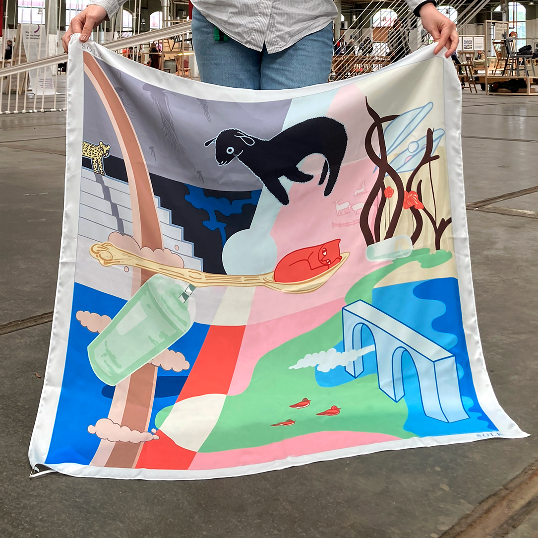 Person holding a colorful scarf with artistic design of animals and landscapes.